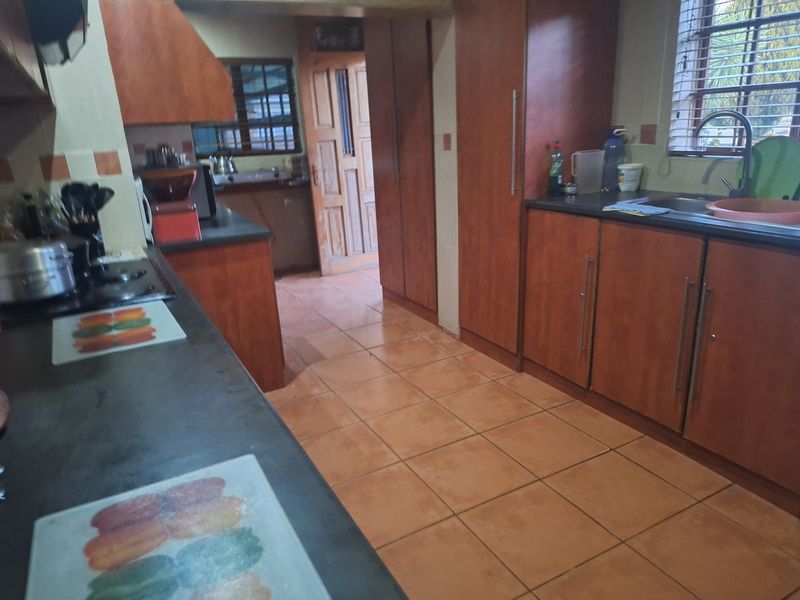 A functional kitchen featuring wooden cabinetry, dark countertops, ceramic tile flooring, and a built-in hob with an extractor fan.