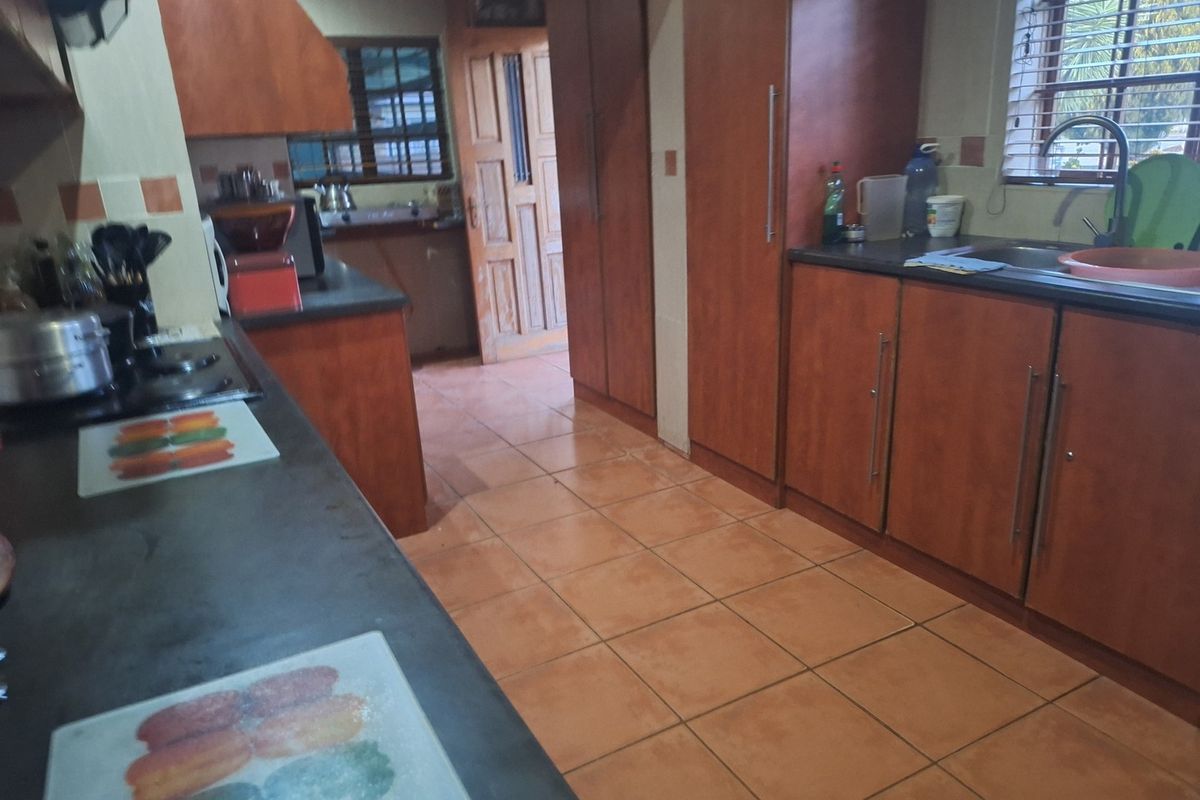 A functional kitchen featuring wooden cabinetry, dark countertops, ceramic tile flooring, and a built-in hob with an extractor fan.