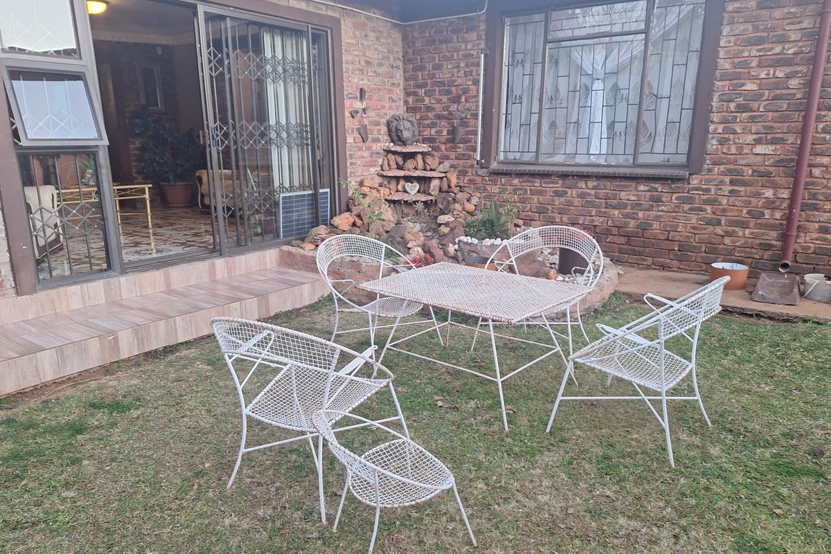 Rear exterior view featuring a face brick facade, tiled patio area, and a stone water feature with access to the interior via sliding doors.