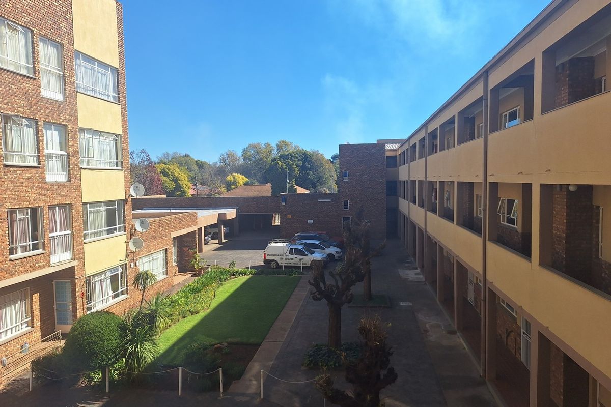 An elevated view of an apartment complex courtyard featuring brick facades, paved walkways, a central garden area, and covered building access.