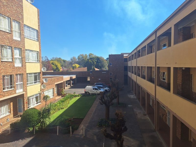 An elevated view of an apartment complex courtyard featuring brick facades, paved walkways, a central garden area, and covered building access.