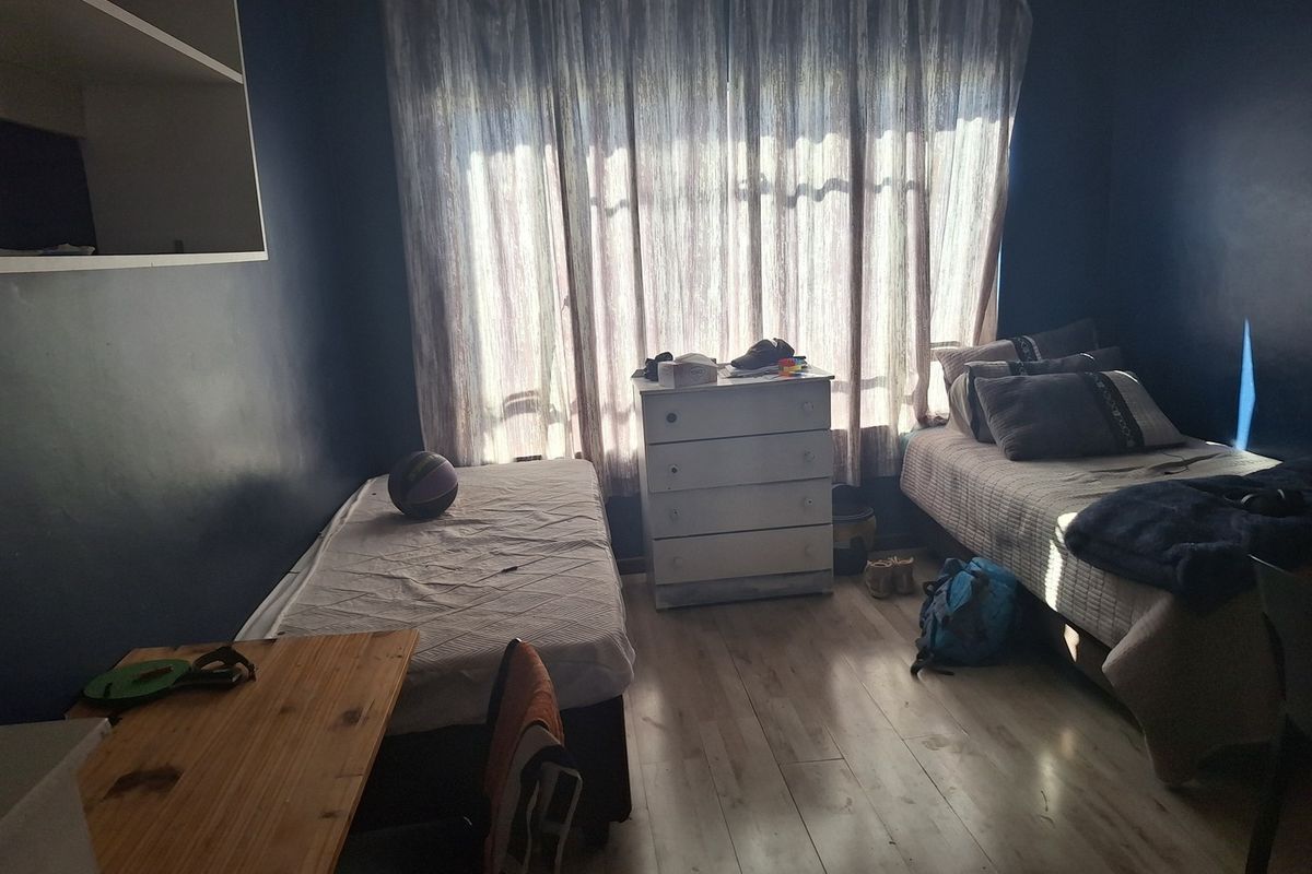 A bedroom featuring laminate flooring and built-in shelving, currently furnished with two beds and a chest of drawers.