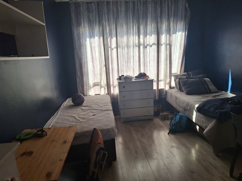 A bedroom featuring laminate flooring and built-in shelving, currently furnished with two beds and a chest of drawers.