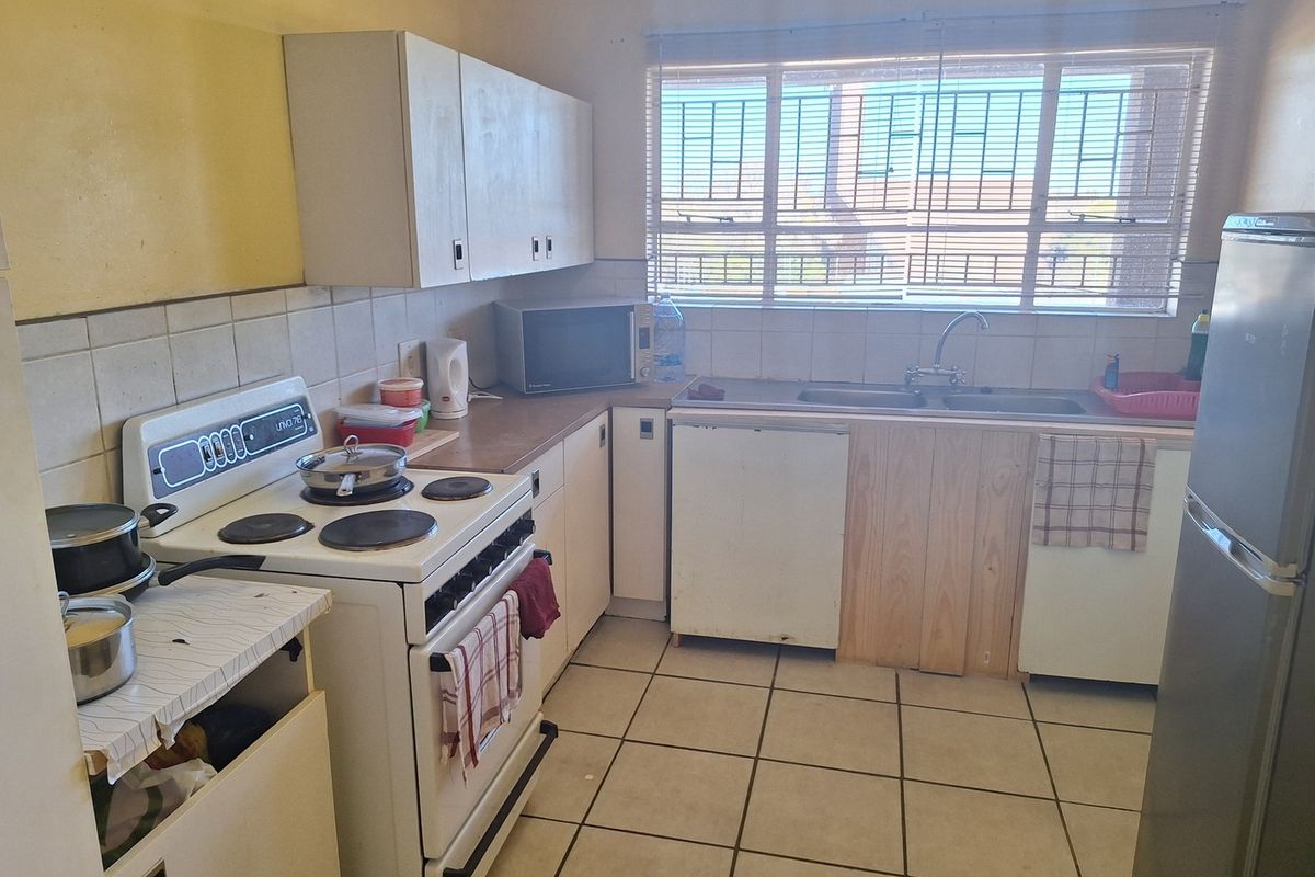 A functional kitchen featuring tiled flooring, a double basin sink, built-in cabinetry, and a tiled backsplash, offering potential for modernization.