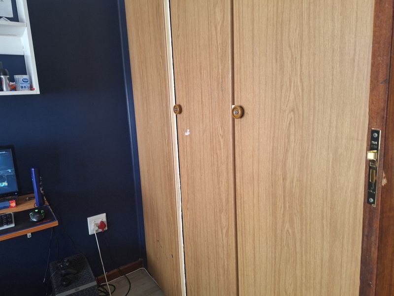 A bedroom featuring a built-in wooden wardrobe with a dark blue accent wall and standard electrical fixtures.