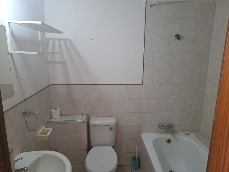 A functional bathroom featuring a standard bathtub, toilet, and washbasin with neutral wall tiling, offering potential for modernization and cosmetic updates.
