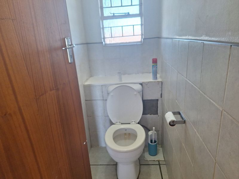 A small bathroom featuring tiled walls and flooring, equipped with a standard toilet and a window with security bars, requiring minor cosmetic repairs.