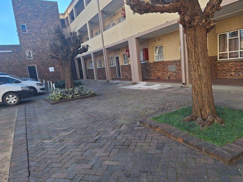 Exterior view of an apartment complex featuring a paved driveway, covered walkways, and established tree beds in a residential setting.