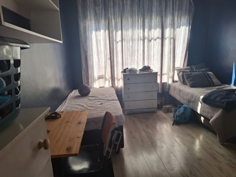 A bedroom featuring laminate flooring and built-in shelving, currently utilized as a multi-bed space with dark blue wall finishes.