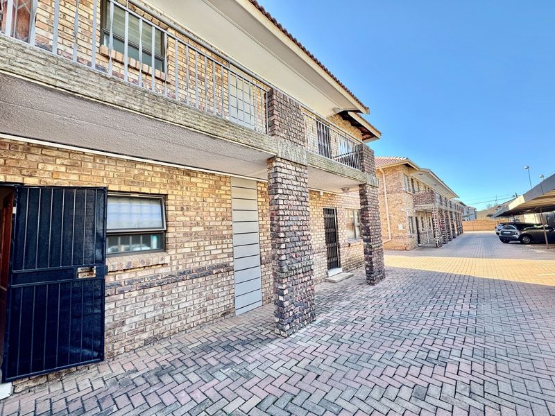 Exterior view of a face brick apartment complex featuring paved driveway access, covered balconies, and dedicated carport parking.