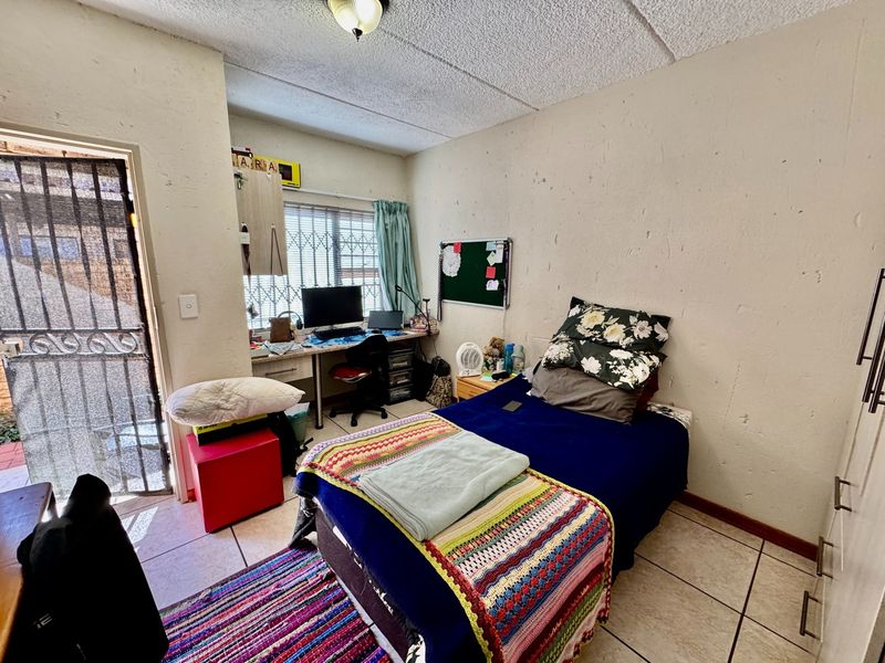 A bedroom featuring tiled flooring, a built-in desk, and a security gate leading to the exterior. The room requires cosmetic updates to wall finishes.
