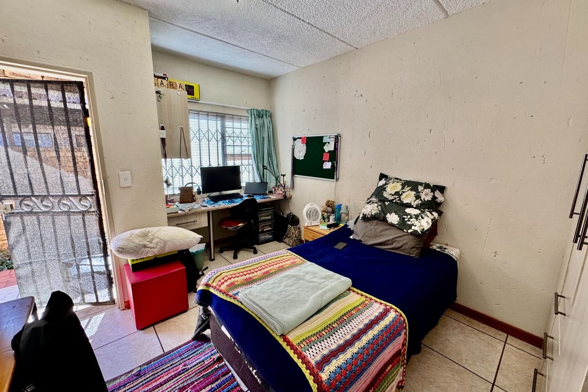A bedroom featuring tiled flooring, a built-in desk, and a security gate leading to the exterior. The room requires cosmetic updates to wall finishes.