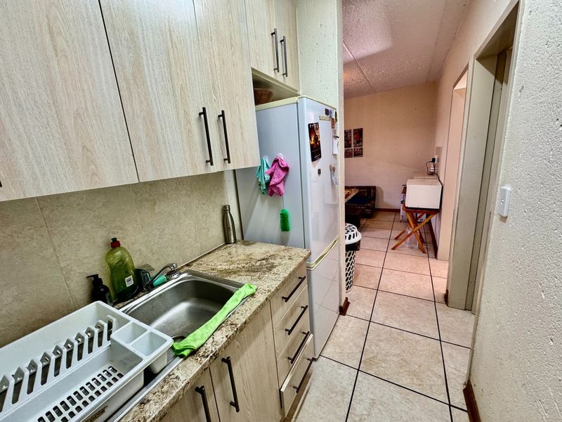 Compact kitchen featuring light wood-look cabinetry, granite countertops, and a stainless steel sink, leading into an adjacent living area.