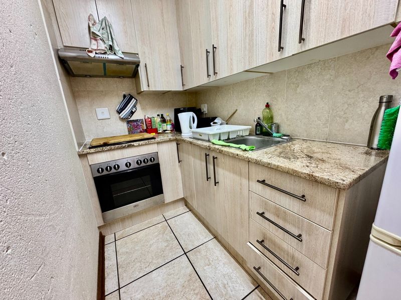 Compact kitchen featuring light wood-finish cabinetry, granite countertops, a built-in oven with extractor fan, and tiled flooring.