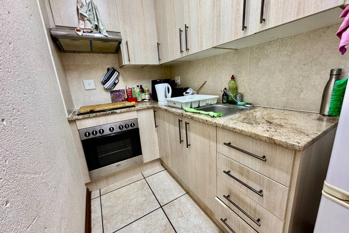 Compact kitchen featuring light wood-finish cabinetry, granite countertops, a built-in oven with extractor fan, and tiled flooring.