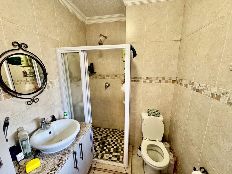 A functional bathroom featuring a shower enclosure, vanity cabinet with a vessel sink, and a toilet, finished with neutral wall and floor tiling.