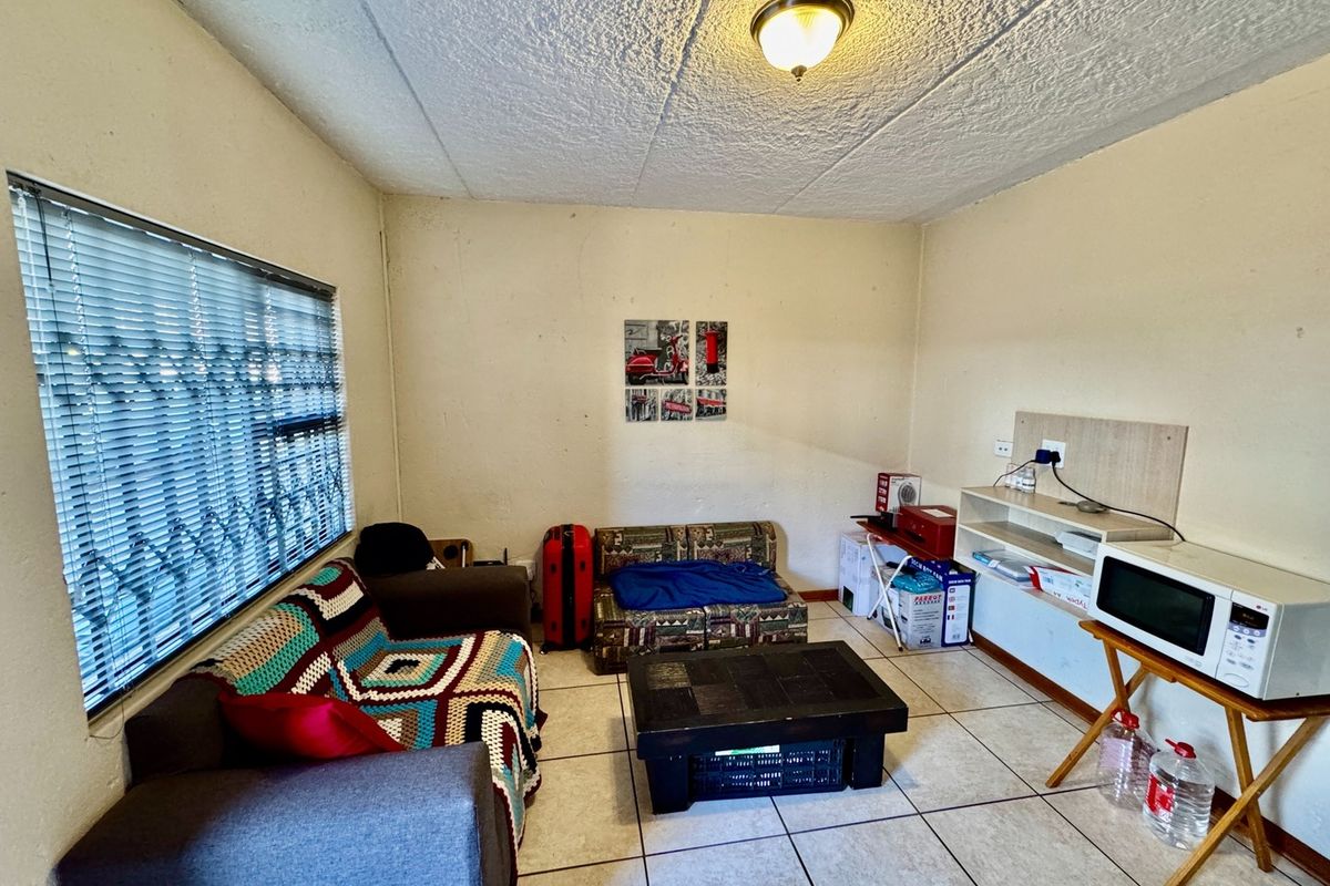 A living area featuring tiled flooring, textured ceilings, and a window with security bars. The space requires cosmetic updates to improve its overall condition.