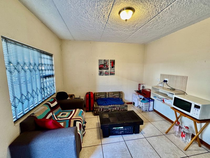 A living area featuring tiled flooring, textured ceilings, and a window with security bars. The space requires cosmetic updates to improve its overall condition.
