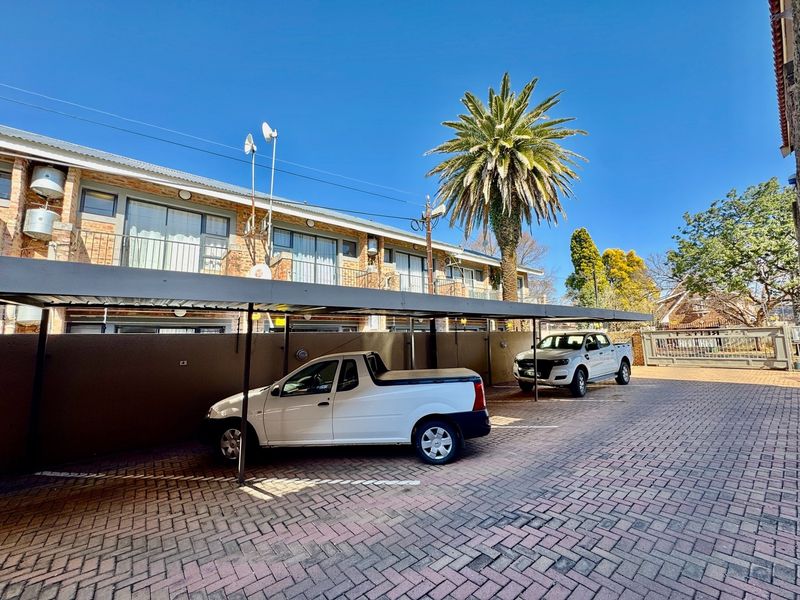 Exterior view of the apartment complex featuring a paved parking area with covered carports and upper-level balconies.