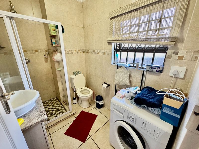 A functional bathroom featuring a shower enclosure, toilet, and vanity basin with neutral wall and floor tiling.