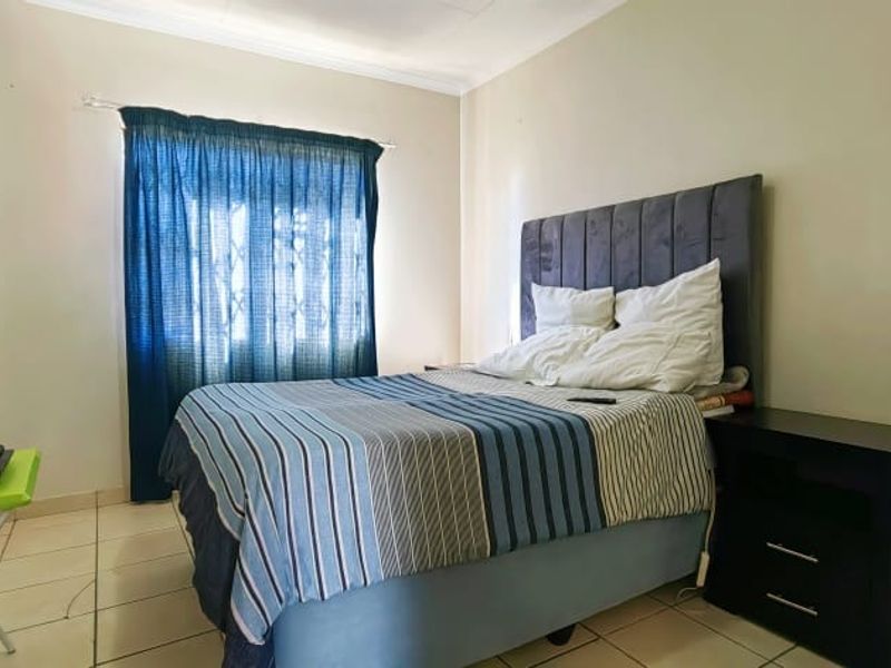 A functional bedroom featuring tiled flooring, a window with security bars, and coving detail.
