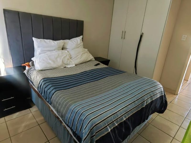 A bedroom featuring tiled flooring and built-in cupboards, with a view leading into an adjacent hallway and utility area.