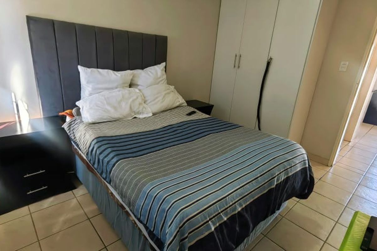 A bedroom featuring tiled flooring and built-in cupboards, with a view leading into an adjacent hallway and utility area.