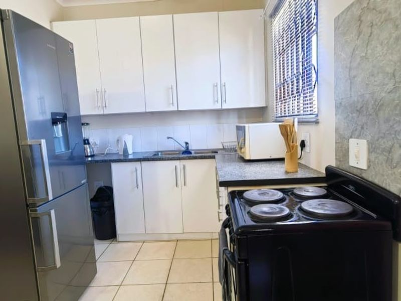 Functional kitchen featuring white cabinetry, laminate countertops, tiled splashback, and a freestanding electric stove with tiled flooring.