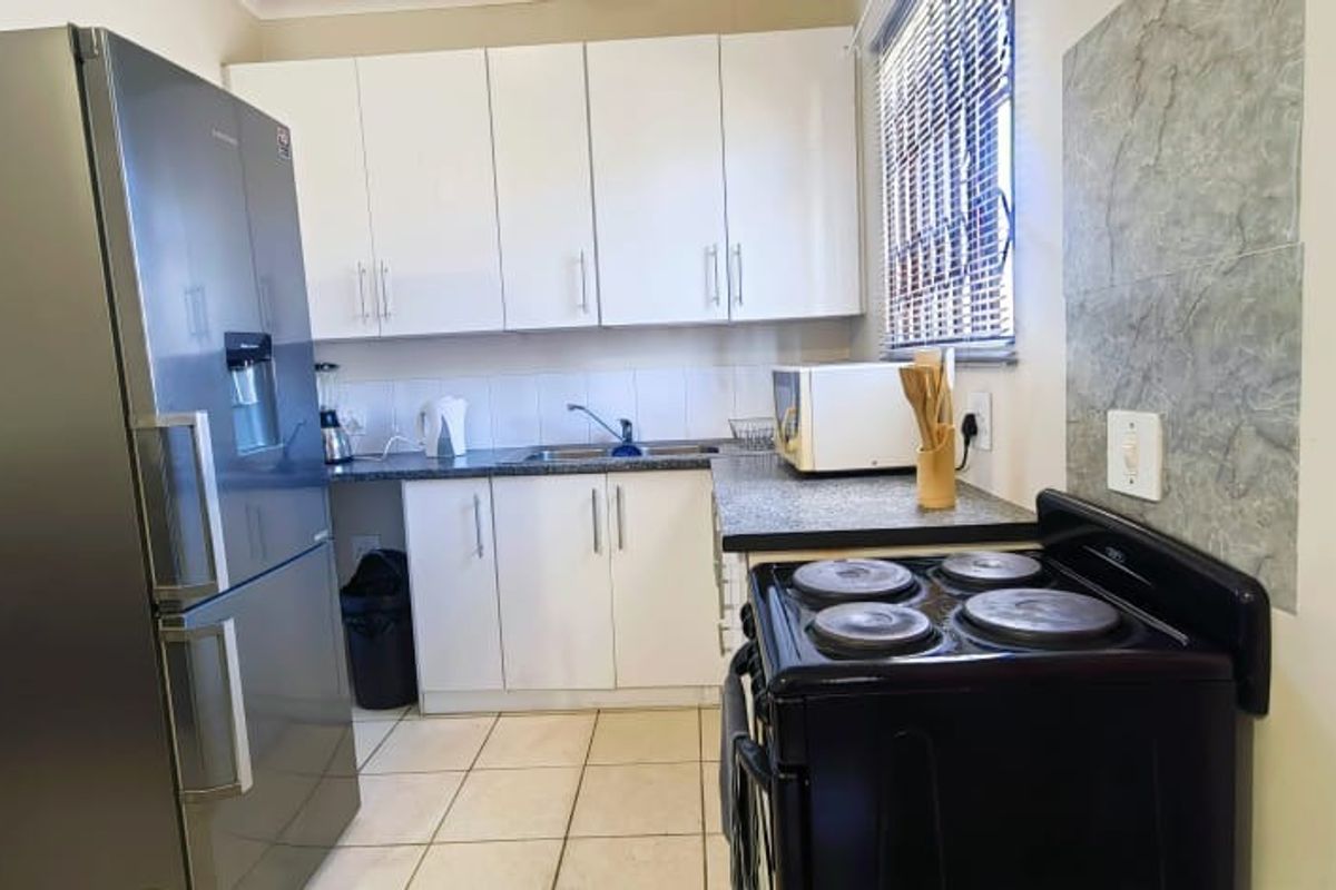 Functional kitchen featuring white cabinetry, laminate countertops, tiled splashback, and a freestanding electric stove with tiled flooring.