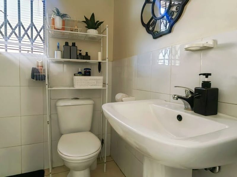 A functional bathroom featuring a pedestal basin, toilet, and bathtub with tiled walls and a security-fitted window.