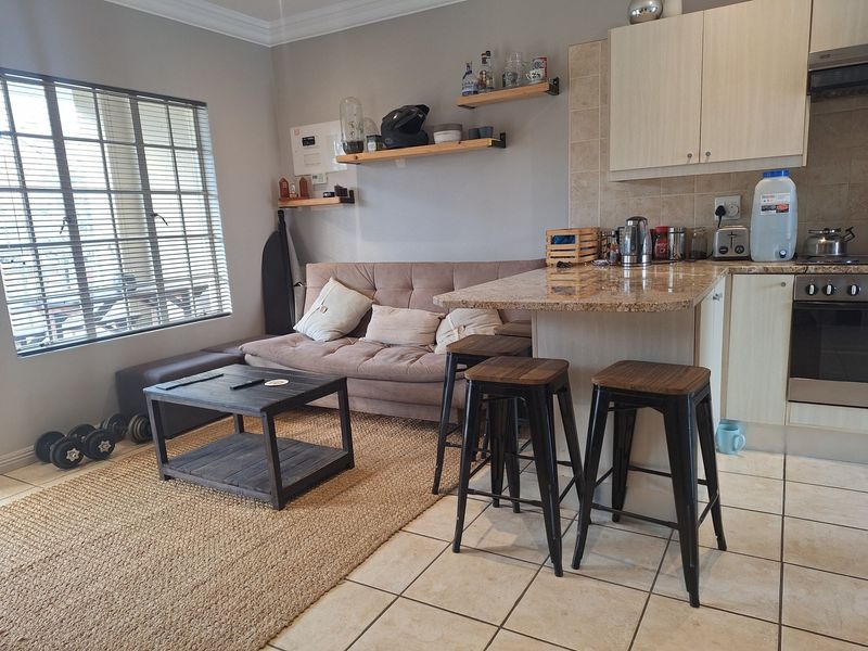 Open-plan living area featuring a compact kitchen with granite countertops, built-in oven, hob, and tiled flooring, seamlessly connected to a comfortable lounge space.