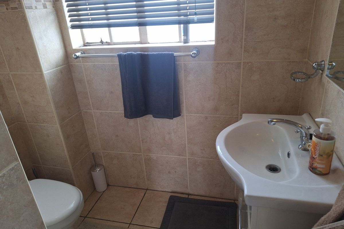 A compact bathroom featuring neutral ceramic wall and floor tiles, a pedestal washbasin with chrome fixtures, and a standard toilet.