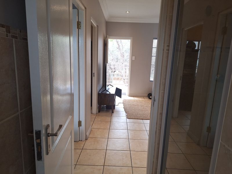 A tiled hallway connecting interior spaces, featuring neutral wall tones and recessed lighting, leading towards an exterior balcony access point.