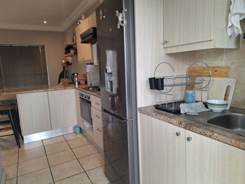 A functional kitchen featuring light wood-finish cabinetry, granite countertops, tiled flooring, and integrated appliances including an oven and extractor fan.