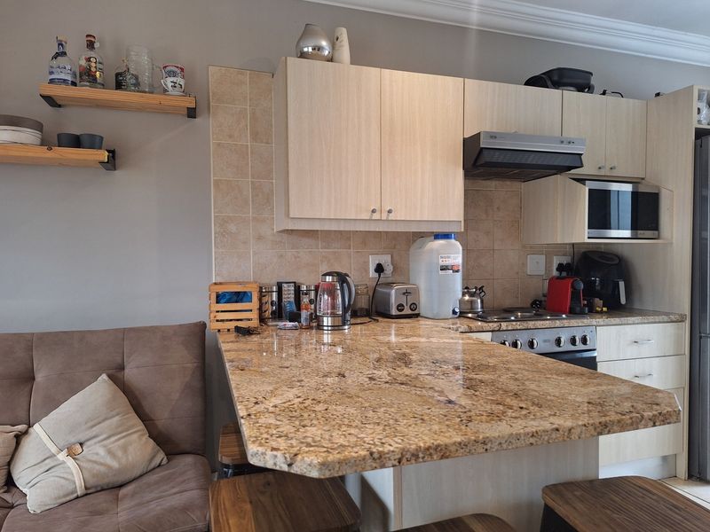 A functional kitchen featuring light wood cabinetry, granite countertops, a tiled backsplash, and integrated appliances, complemented by decorative floating wall shelves.