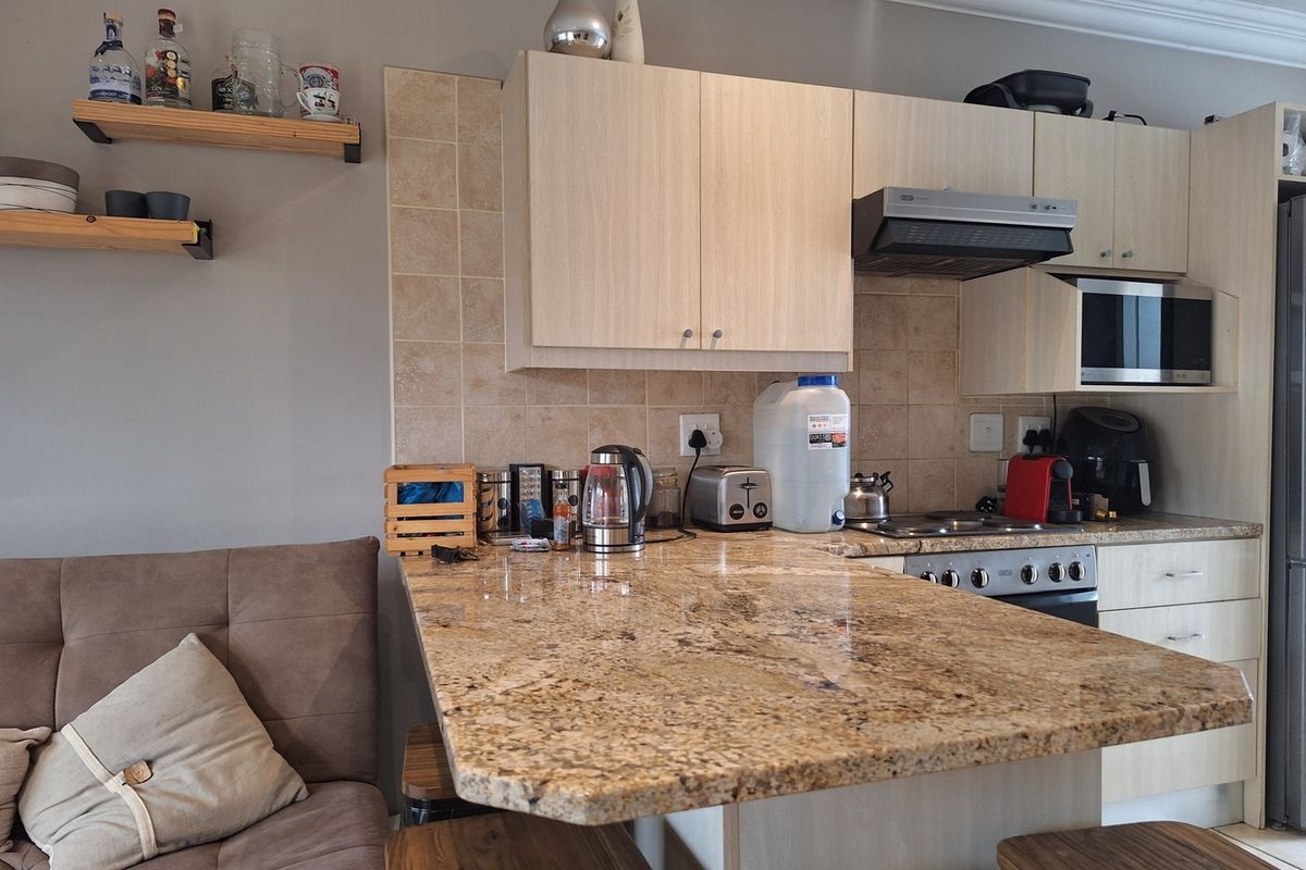 A functional kitchen featuring light wood cabinetry, granite countertops, a tiled backsplash, and integrated appliances, complemented by decorative floating wall shelves.