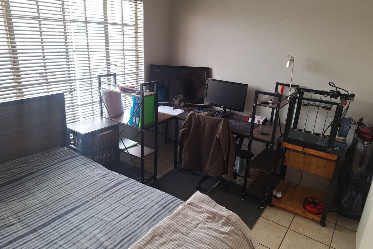 A functional bedroom featuring tiled flooring and venetian blinds, currently utilized as a combined sleeping and workspace area.