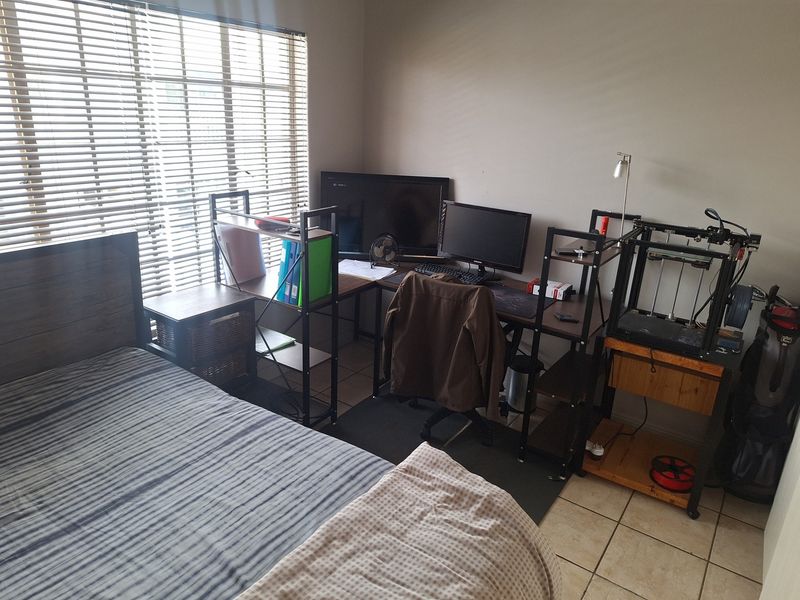 A functional bedroom featuring tiled flooring and venetian blinds, currently utilized as a combined sleeping and workspace area.