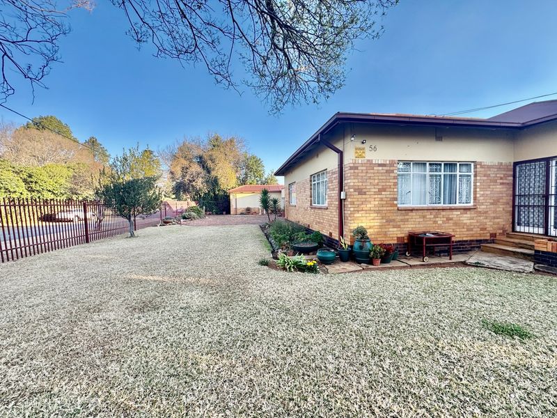 Front view of a brick-faced house featuring a spacious lawn, metal perimeter fencing, and a secure entrance gate.