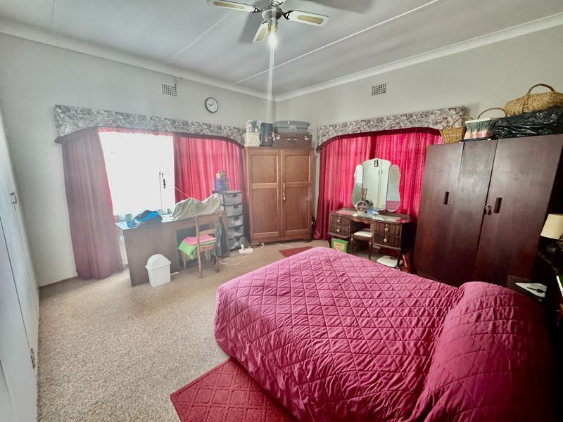 A spacious bedroom featuring built-in cupboards, a ceiling fan, and large windows with traditional pelmets.