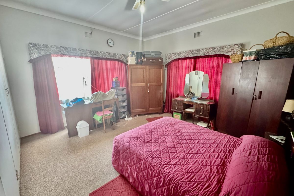 A spacious bedroom featuring built-in cupboards, a ceiling fan, and large windows with traditional pelmets.