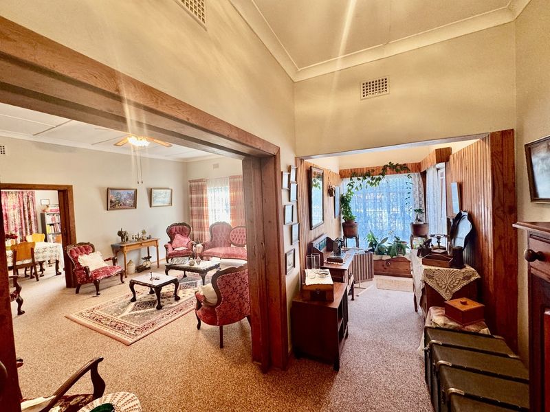 Spacious living area featuring timber door frames, wood paneling, and a ceiling fan, offering a traditional layout with connected living spaces.