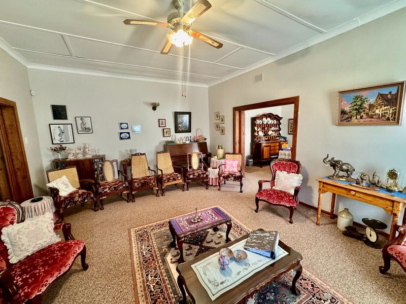 A spacious living room featuring a ceiling fan and carpeted flooring, with an open doorway leading to an adjacent dining area.