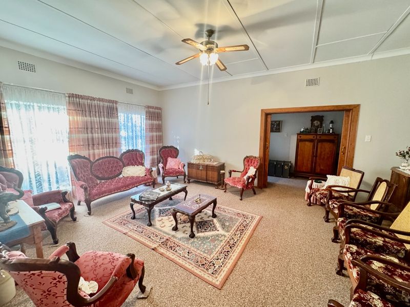 Spacious living room featuring carpeted flooring, a ceiling fan, and large sliding glass doors providing natural light, with a timber-framed opening to an adjacent room.
