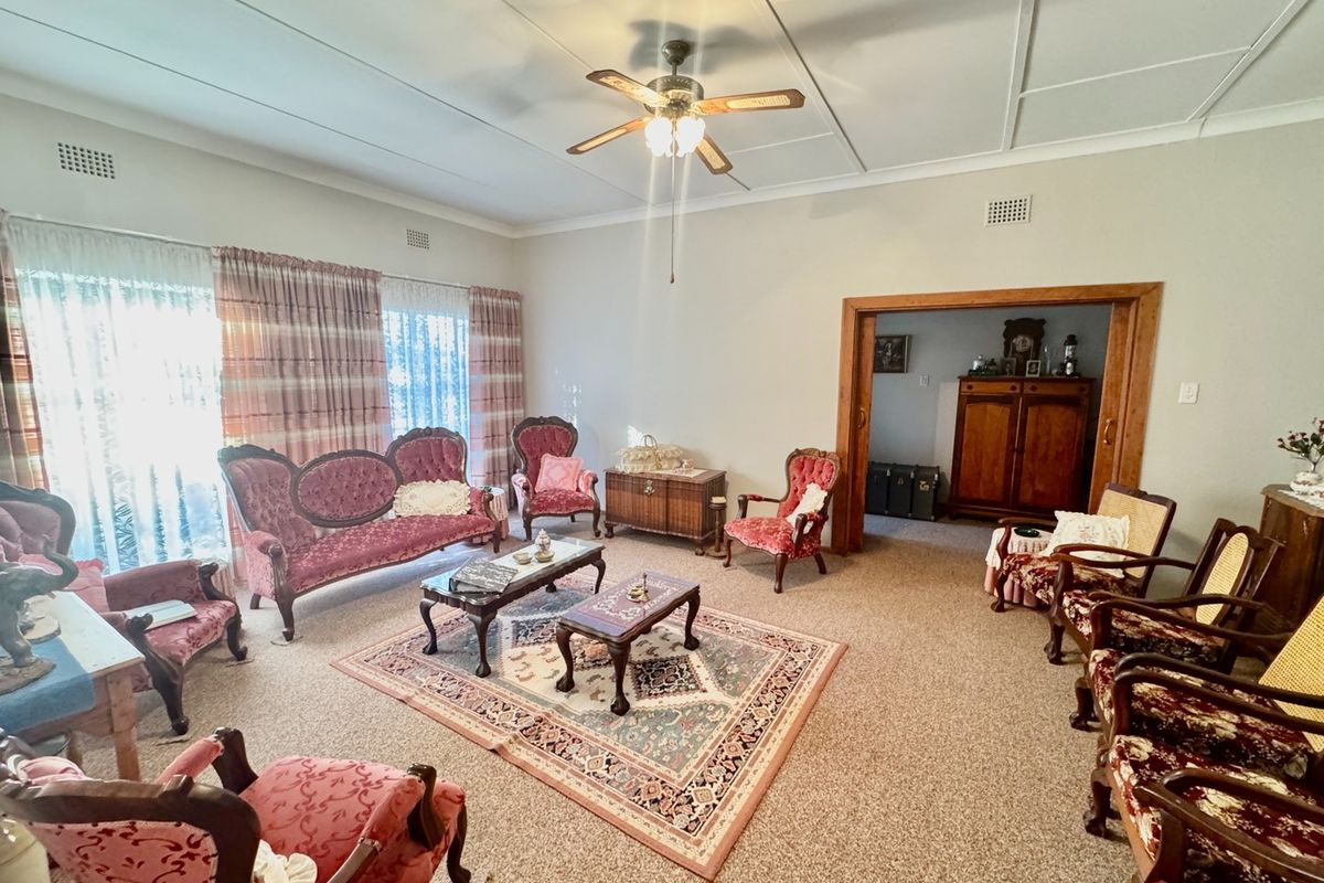 Spacious living room featuring carpeted flooring, a ceiling fan, and large sliding glass doors providing natural light, with a timber-framed opening to an adjacent room.