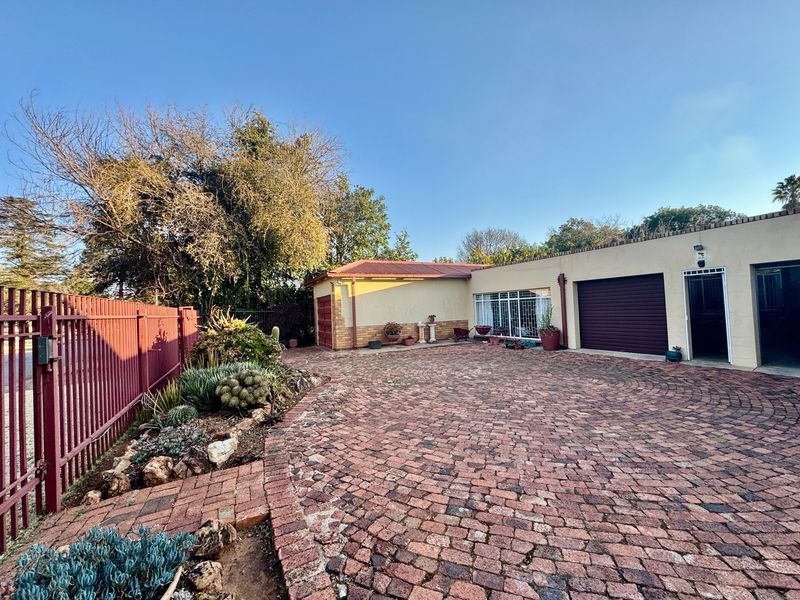 Front exterior view featuring a brick paved driveway, secure metal fencing, and a garage with a roll-up door.