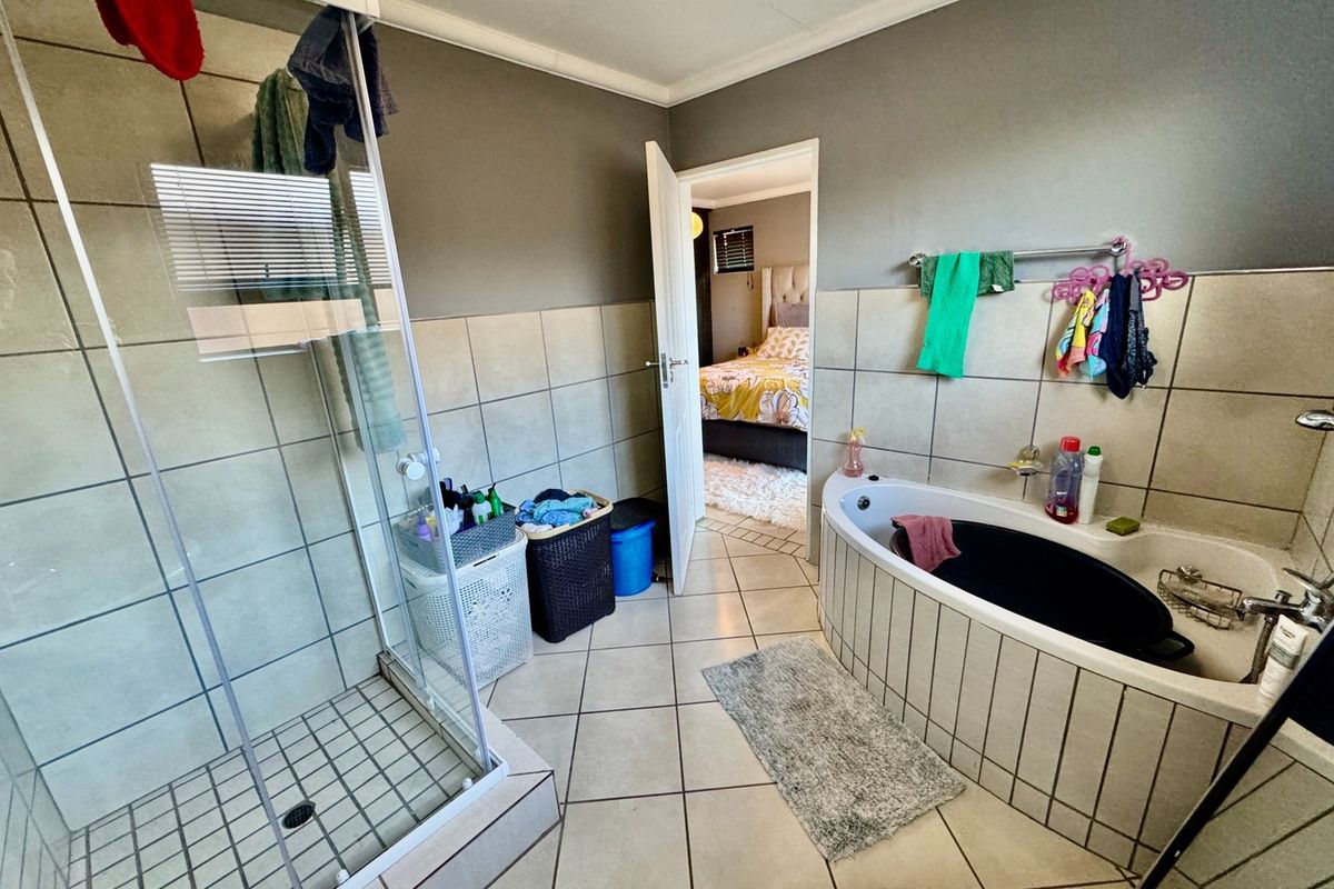 A functional bathroom featuring a glass-enclosed shower, a built-in corner bathtub, and neutral wall and floor tiling.