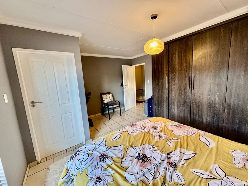 A bedroom featuring built-in dark wood cupboards, tiled flooring, and a coved ceiling, providing a functional and neutral living space.