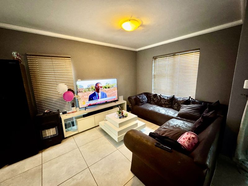 A living room featuring large format floor tiles, neutral wall paint, and venetian blinds on the windows.