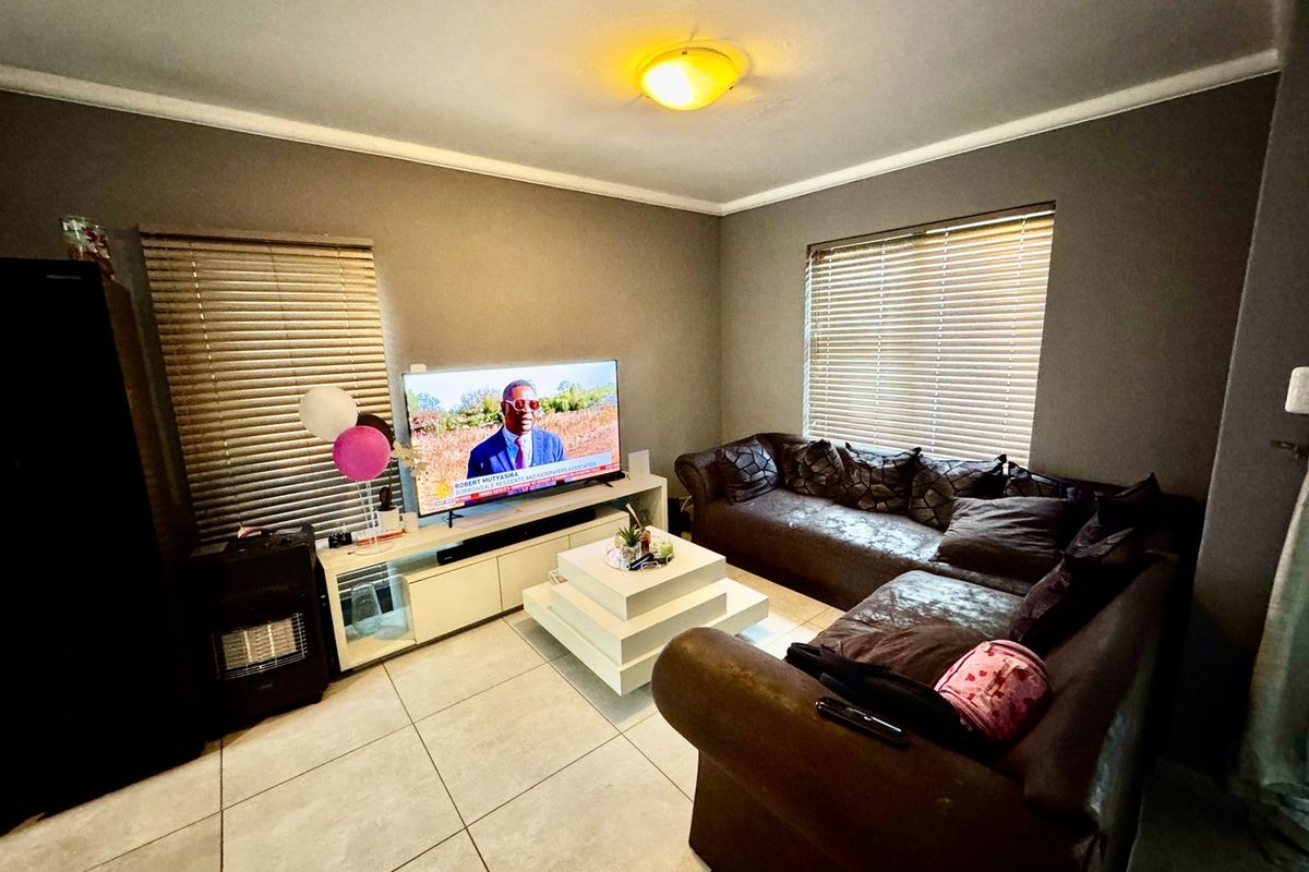 A living room featuring large format floor tiles, neutral wall paint, and venetian blinds on the windows.